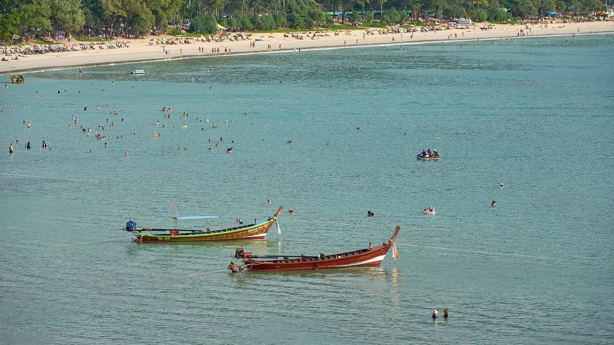 Kata Beach with long-tail boats and umbrellas — the family-tourism bay shared by the Karon and Kata condo market